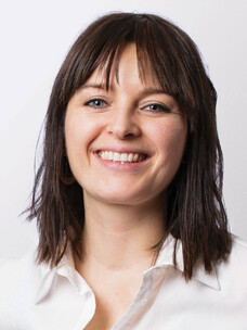 Katja Lesser mit schulterlangem dunklem Haar und weißer Bluse, lächelnd.